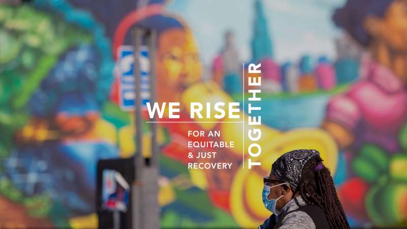 Image text: We Rise Together. A Black woman in a face mask contemplates a mural in Chicago.