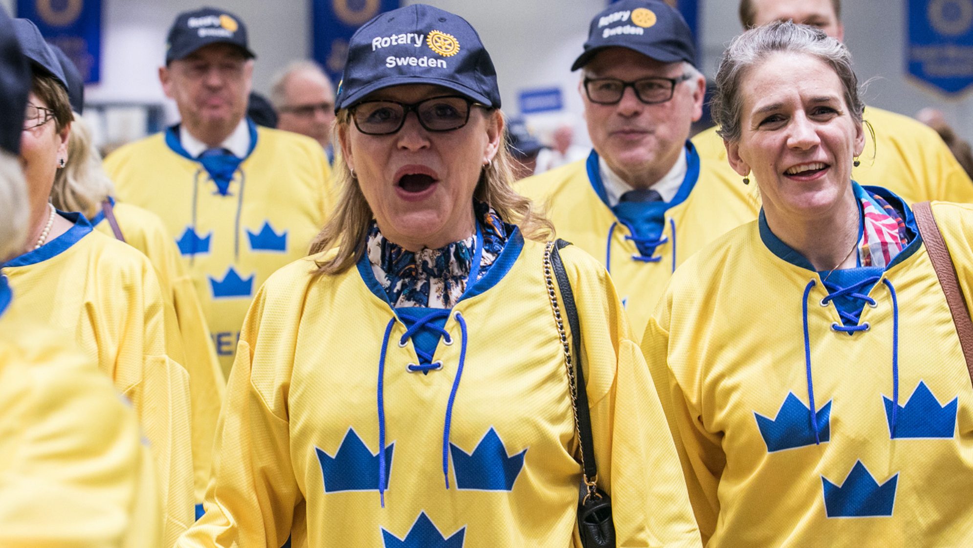 Crowd wearing yellow shirts and blue hats with Rotary Sweden logo.