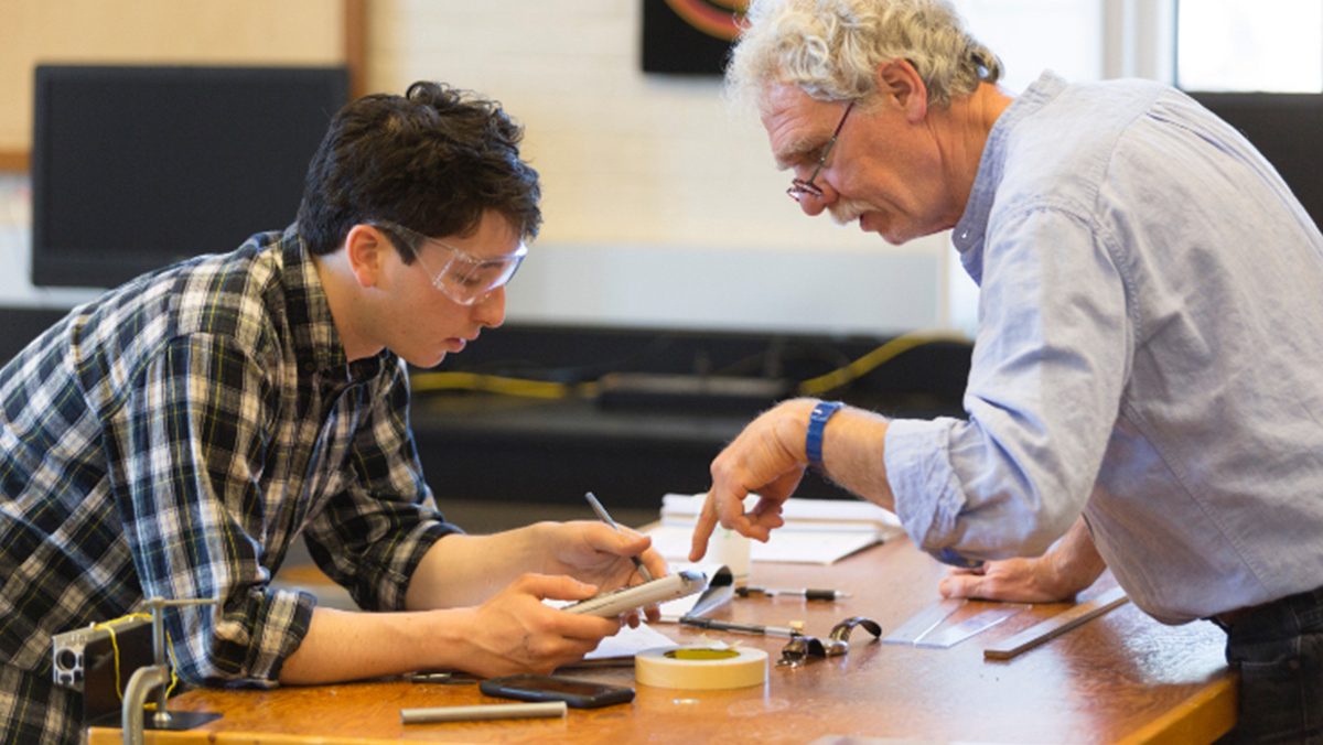An instructor and a student examine a disassembled mechanical device.