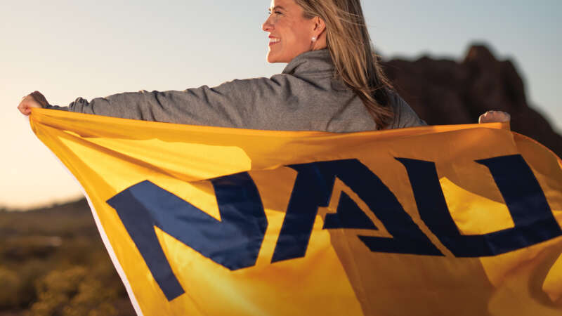 Woman in AZ landscape with NAU flag–Reconnecting with NAU